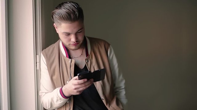 Serious focused phone user texting message. Young man with stylish haircut holding smartphone in open folio case and typing with one hand. Communication concept