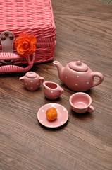 A porcelain spotted tea set with a pink basket and an orange rose