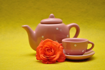A teacup and a kettle with an orange rose on a yellow background