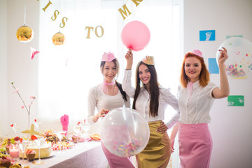 The cheerful young stewardesses standing near the festive table at the hen party and holding balloons in hands