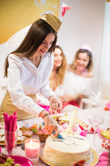 The beautiful young bride stewardess standing near the festive table at the hen party and cutting a cake