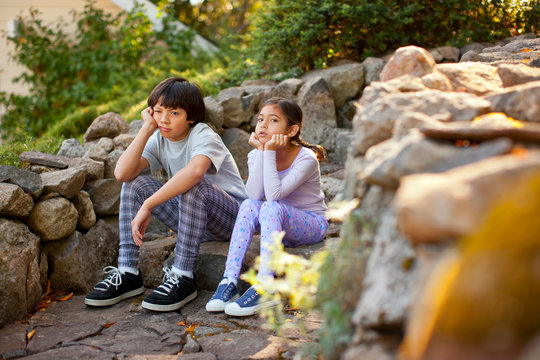 Unhappy brother and sister sitting next to each other on a stone step.