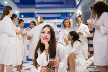 The attractive bride sitting near her friends at the hen party near a pool and holding a glass of champagne