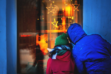 An adult with a child looks into a luminous Christmas window. Dream concept