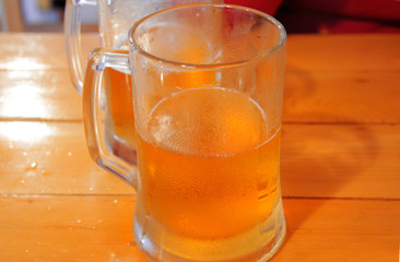 Transparent glass mug with beer on wooden table in cafe