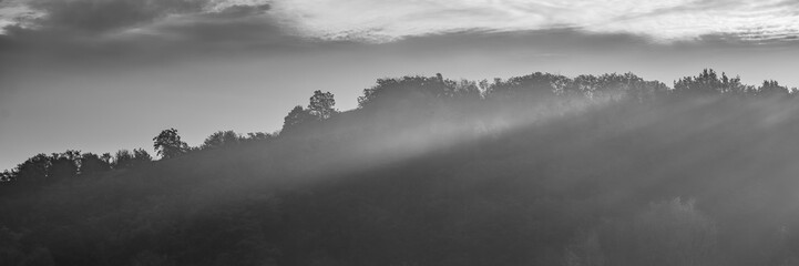 sun rays against the background of clouds and forest in a hilly area, rural landscape. Web banner.