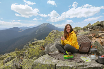 Fototapeta premium Young woman in yellow jacket have a picnic on top of the mountain. 