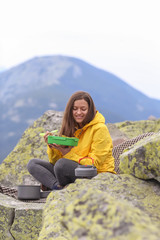 Naklejka na ściany i meble Young woman in yellow jacket have a picnic on top of the mountain. 