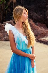 Young beautiful caucasian blonde woman in long tull butterfly white blue dress on coast of sea.female running towards the ocean freedom