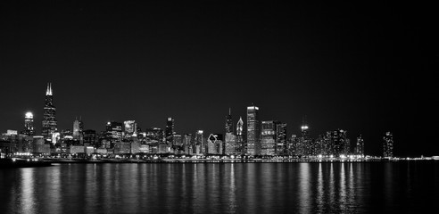 Long-exposure photo of downtown Chicago at night. The light of the stars can be see in the clear sky above, and the reflection of the city lights is in the lake in the foreground.