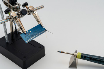 Blue circuit board in soldering helping hands (third hand or auxiliary clip tool) before technological soldering process with soldering iron 