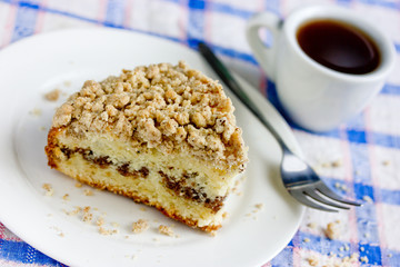 Traditional cinnamon coffee cake piece on a plate and cup of coffee on table