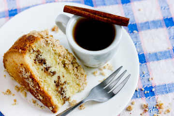 Traditional cinnamon coffee cake piece on a plate and cup of coffee on table