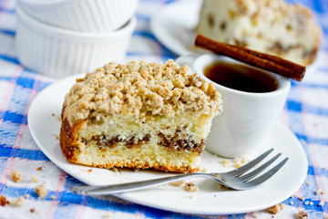 Traditional cinnamon coffee cake piece on a plate and cup of coffee on table