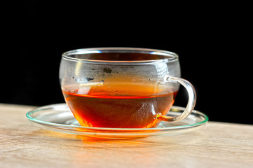 Transparent cup with black tea and saucer. The light surface of the table. dark background. Close-up.