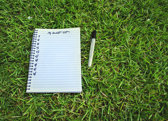 Notebook bucket list on grass background.