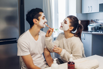 Woman applying clay mask on her boyfriend's face. Young loving couple taking care of skin at home