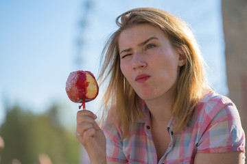 pretty young woman eating and biting red caramel apple in the park in the sunny day