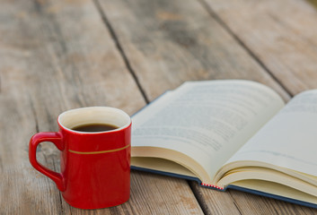 Cup of coffee with open book on wooden background