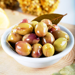 Green olives in bowl with daphne leaves and lemon on wooden background