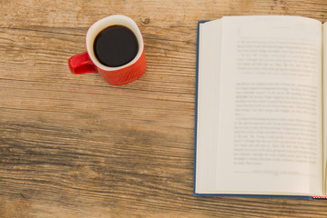 Cup of coffee with open book on wooden background.