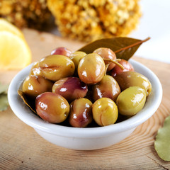 Green olives in bowl with daphne leaves and lemon on wooden background