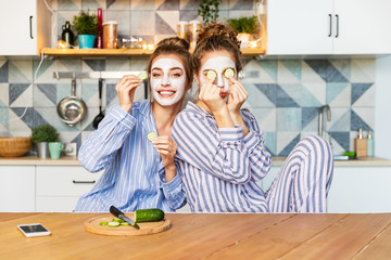 Portrait of carefree young models posing on kitchen in striped comfy pyjamas and having fun on nice interior. Youth skincare and friendship concept. Blurred background
