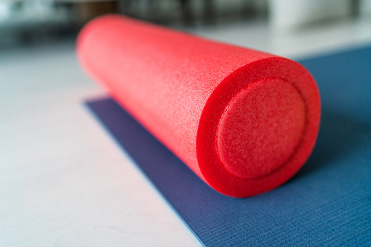 Foam roller fitness equipment on exercise mat gym floor. Indoors closeup of sports object, accessory for athletes to massage tired and tense muscles.