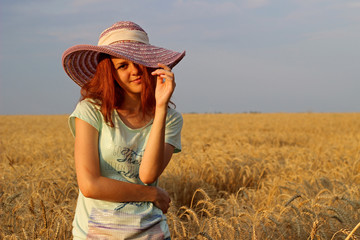 Girl in a hat on yellow wheat field in summer