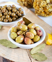 Green olives in bowl with lemons and daphne leaves.