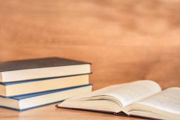 Open book with pile of closed books on wooden background.