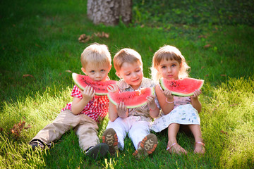 Funny kids eating watermelon outdoors in summer park.