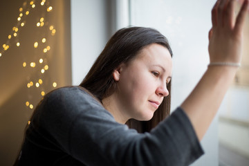 Fototapeta premium Pretty young brunette woman looking from the window, looking sad