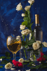 Valentines day. Splash of white wine. Romantic evening. Wine, a bunch of white roses and red hearts on a blue background. Holiday of lovers. A delicious alcoholic drink for two people. Picture photo.