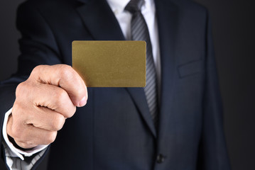 Businessman holding a blank gold card in front of his toso.