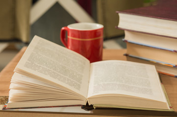 Pile of closed books and open book with cup of coffee on wooden background.