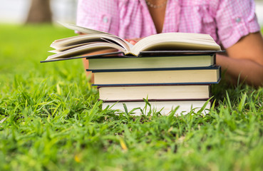 Woman reading an open book on the grass with pile of books on the  background.