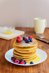 American pancakes with berries, honey and powdered sugar on a wooden table