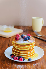 American pancakes with berries, honey and powdered sugar on a wooden table