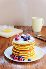 American pancakes with berries, honey and powdered sugar on a wooden table