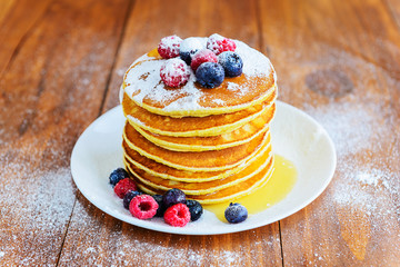 American pancakes with berries, honey and powdered sugar on a wooden table