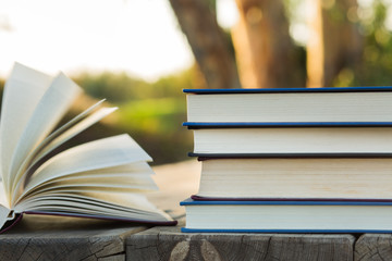 Pile of closed book with open book outdoors on wooden background
