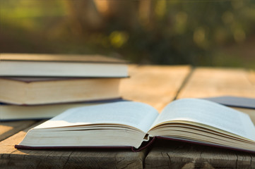Pile of closed book with open book outdoors on wooden background