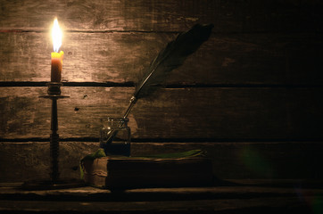 Quill pen in a inkpot and book in the light of burning candle on the writer desk background....