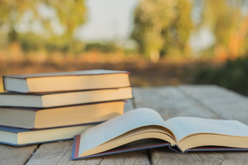 Pile of closed book with open book outdoors on wooden background