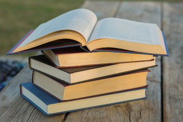 Pile of closed book with open book outdoors on wooden background