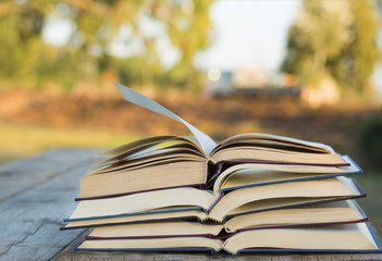 Pile of closed book with open book outdoors on wooden background