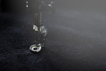 Extreme close up view on needle and embroidery foot of a modern sewing machine stitching with golden yarn on black soft fabric - dark misty light mood - Powered by Adobe
