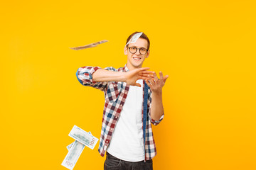 happy man, wearing glasses and a plaid shirt, throwing out money banknotes on a yellow background