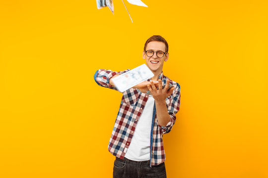 happy man, wearing glasses and a plaid shirt, throwing out money banknotes on a yellow background